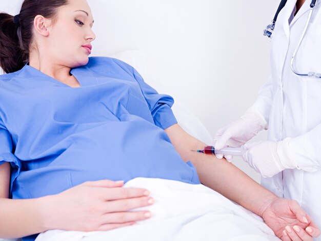 El médico toma sangre en el análisis de una vena de la mujer embarazada