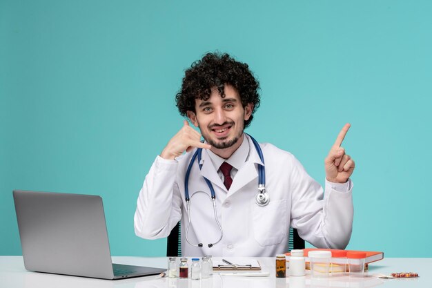 Médico trabajando remotamente en la computadora lindo y guapo doctor en bata de laboratorio haciendo gesto de llamada