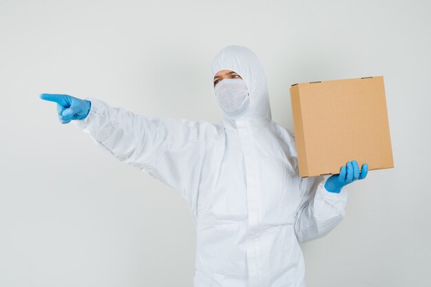 Médico varón apuntando hacia afuera mientras sostiene la caja de cartón en traje protector