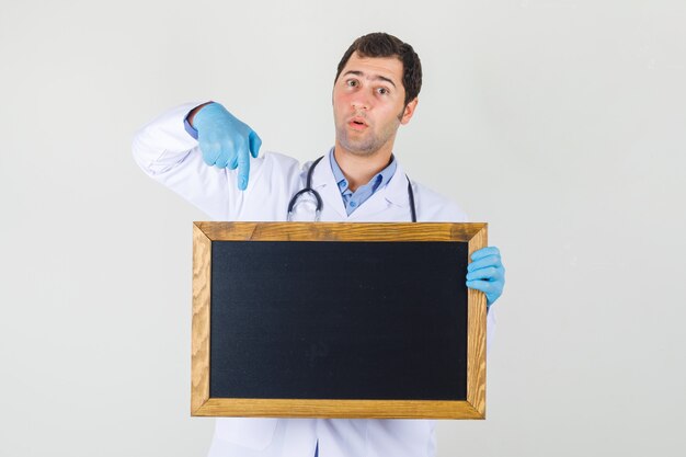 Médico varón apuntando con el dedo a la pizarra en bata blanca, guantes