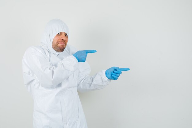 Foto gratuita médico varón apuntando hacia el lado con traje protector, guantes y mirando curioso. vista frontal.