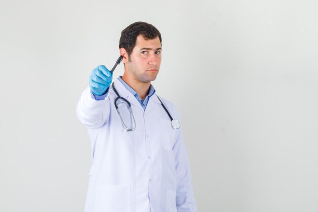 Médico varón apuntando la pluma al frente en bata blanca, vista frontal de los guantes.