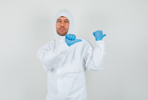 Médico varón apuntando los pulgares hacia el lado en traje protector