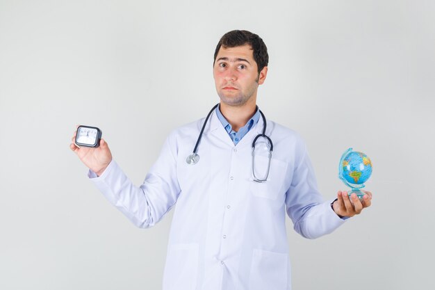 Médico varón en bata blanca con reloj y globo del mundo