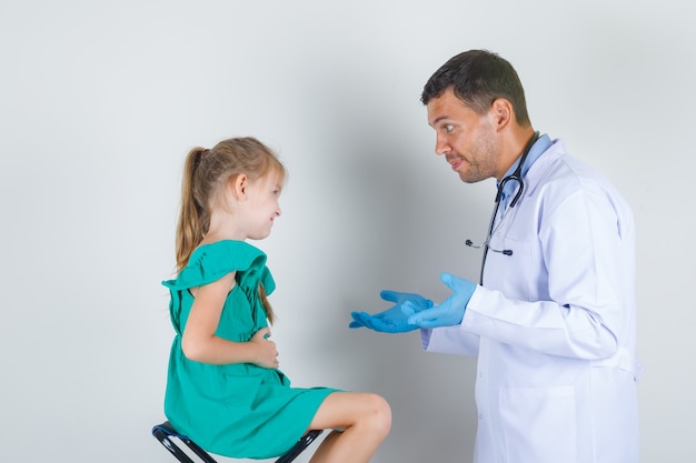 Médico varón en bata blanca tratando de identificar problemas con el niño y mirando con cuidado