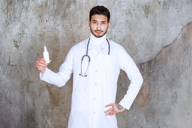 Médico varón con estetoscopio sosteniendo una botella de desinfectante de manos blanco