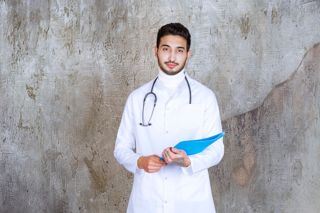 Médico varón con estetoscopio sosteniendo una carpeta azul