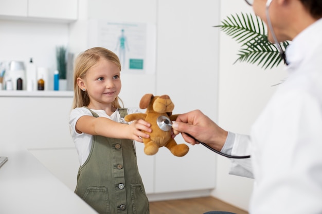 Médico varón examinando el juguete del oso de peluche de la niña durante la cita