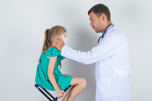 Médico varón con guantes médicos en la sala de examen en uniforme blanco y mirando con cuidado. vista frontal.