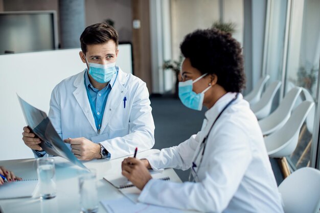 Médico varón hablando con un colega mientras examina la imagen de rayos X en una reunión