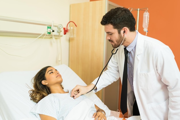 Médico varón hispano que examina al paciente con estetoscopio en el hospital