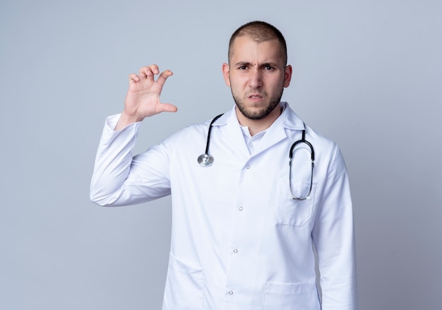 Médico varón joven disgustado con bata médica y un estetoscopio alrededor de su cuello que muestra el tamaño aislado sobre fondo blanco.