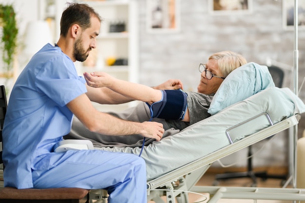 Médico varón joven que toma la presión arterial de una mujer mayor en un hogar de ancianos