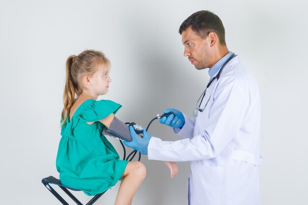 Médico varón midiendo los pulsos del corazón del niño en uniforme blanco, guantes