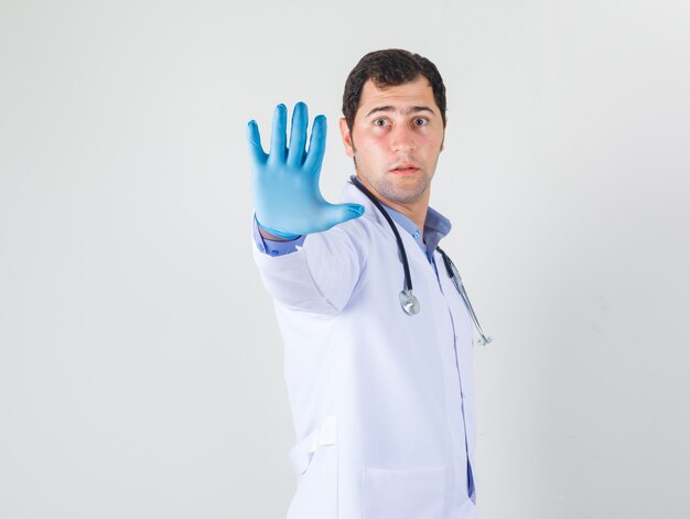 Médico varón mostrando la mano con guantes en bata blanca y mirando con cuidado