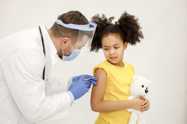 Médico varón vacunando a una niña negra aislada de fondo blanco