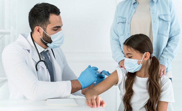 Médico varón vacunando a una niña que es apoyada por su madre