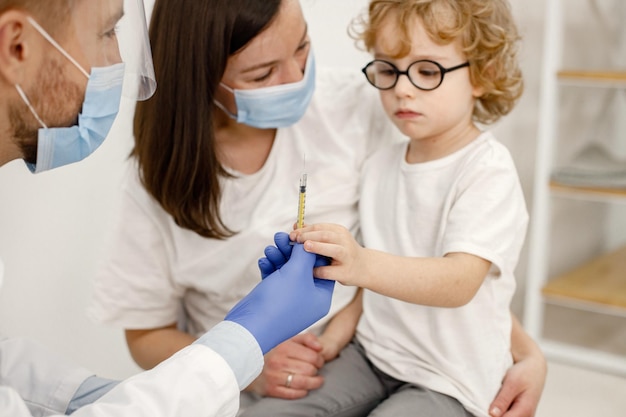 Médico varón vacunando a un niño pequeño sentado en el regazo de la madre