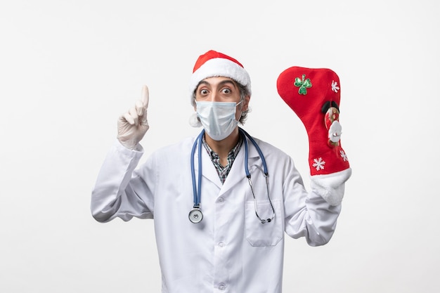 Médico varón de vista frontal con gran calcetín de vacaciones en el escritorio blanco virus covid christmas