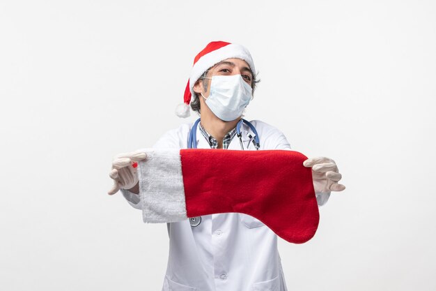 Médico varón de vista frontal sosteniendo un calcetín de vacaciones grande en la pared blanca vacaciones de virus covid