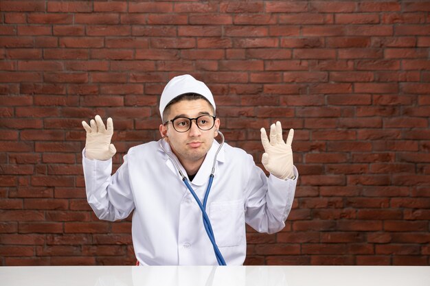 Médico varón de vista frontal en traje médico blanco con estetoscopio