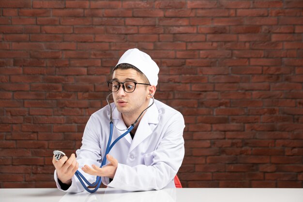 Médico varón de vista frontal en traje médico blanco con estetoscopio