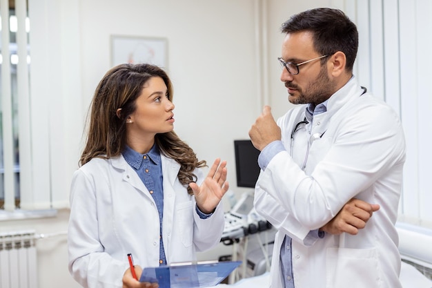 Médicos confiados discutiendo sobre el historial médico Los trabajadores de la salud masculinos y femeninos usan batas de laboratorio Están trabajando en el hospital