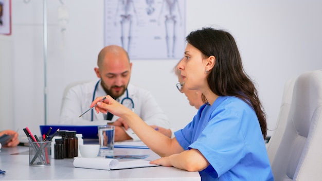 Médicos y enfermeras discutiendo sobre medicina en la sala de reuniones con conferencia médica para resolver problemas de salud sentados en el escritorio. Grupo de médicos hablando sobre los síntomas de la enfermedad en la sala de la clínica