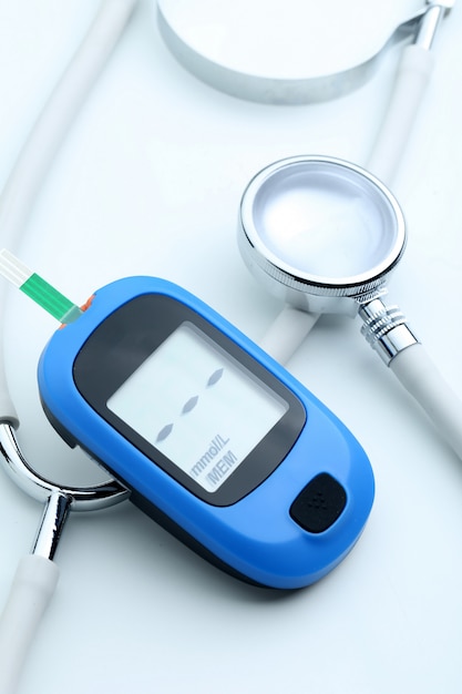 Medidor de glucosa en sangre y estetoscopio sobre fondo blanco