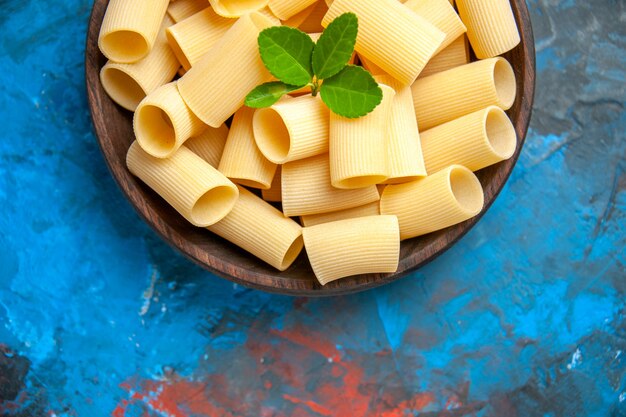 Medio plano de preparación de la cena con fideos de pasta con verde en una olla marrón sobre fondo azul.