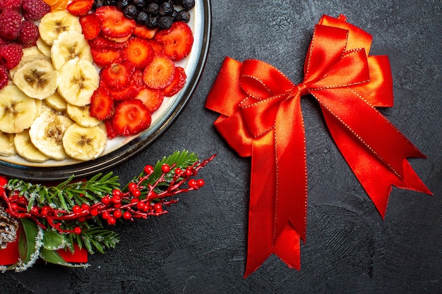 Medio tiro de colección de frutas frescas en accesorios de decoración de plato de cena ramas de abeto y números en una servilleta roja y cinta roja