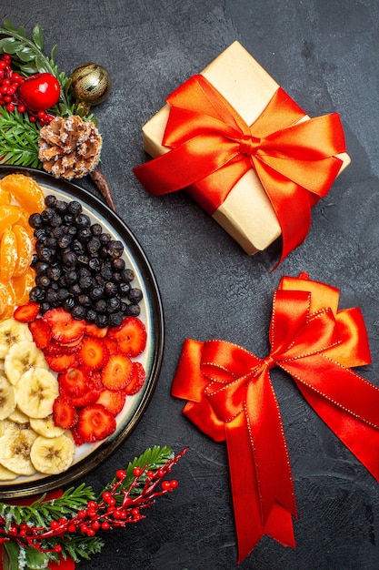 Medio tiro de colección de frutas frescas en accesorios de decoración de plato de cena ramas de abeto y números en una servilleta roja y rbbon rojo y regalo