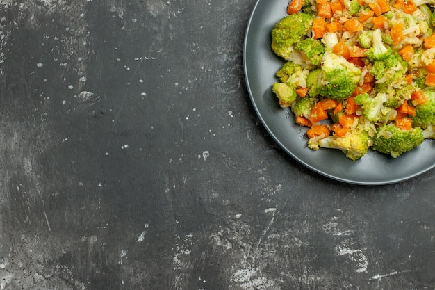 Medio tiro de comida saludable con brocoli y zanahorias en una placa negra sobre tabla gris