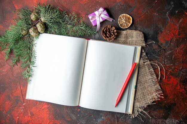 Medio tiro de cuaderno de espiral abierto con pluma roja y ramas de abeto sobre una toalla sobre fondo oscuro