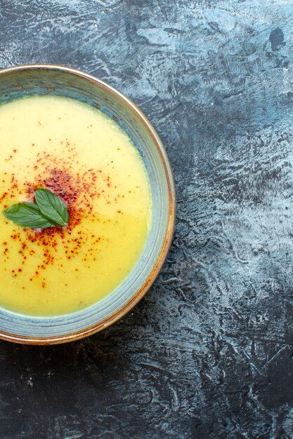 Medio tiro de deliciosa sopa servida con pimienta y menta en una olla azul en el lado derecho sobre fondo oscuro