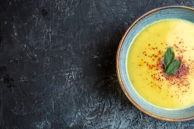 Medio tiro de deliciosa sopa servida con pimienta y menta en una olla azul en el lado izquierdo sobre fondo oscuro