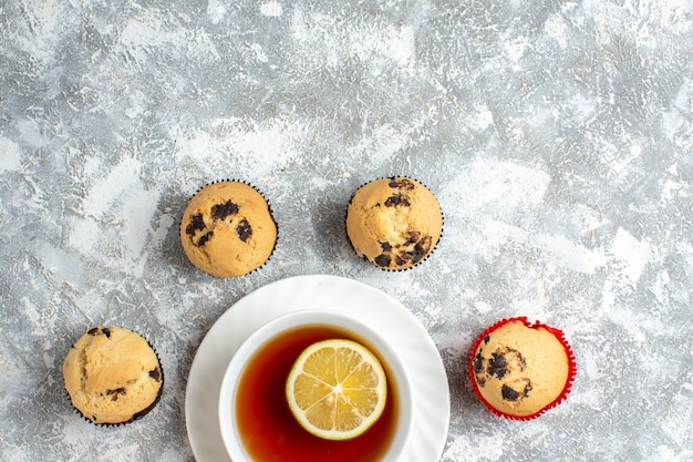 Medio tiro de deliciosos cupcakes pequeños con chocolate alrededor de una taza de té negro sobre la superficie del hielo