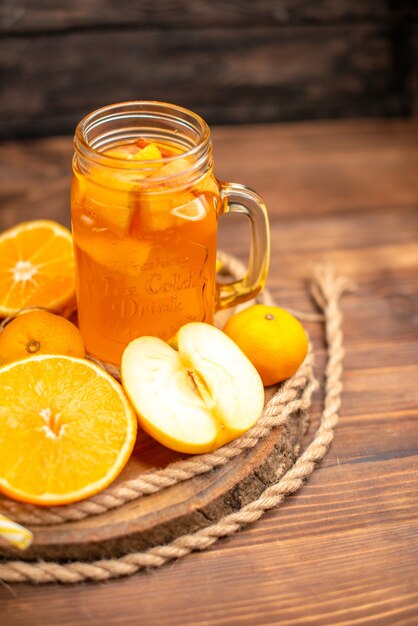 Medio tiro de jugo fresco orgánico en una botella y vaso servido con tubo y frutas sobre una tabla de cortar y sobre una mesa de madera marrón