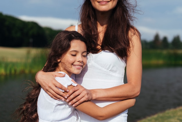 Medio tiro madre e hija abrazando por el lago