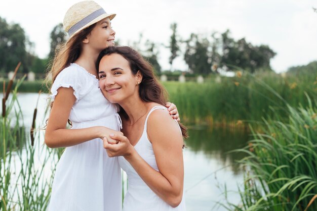 Medio tiro madre e hija abrazando por el lago