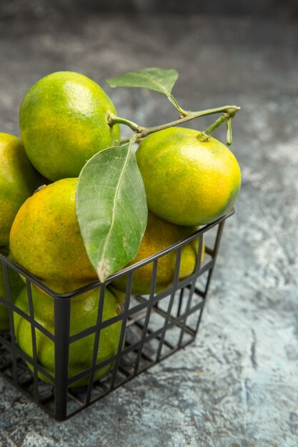 Medio tiro de mandarinas verdes con hojas en una canasta sobre fondo gris