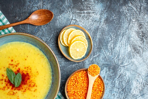 Medio tiro de una olla azul con una sabrosa sopa servida con menta y pimienta junto a una cuchara de madera de limón picado y un guisante amarillo sobre fondo azul.