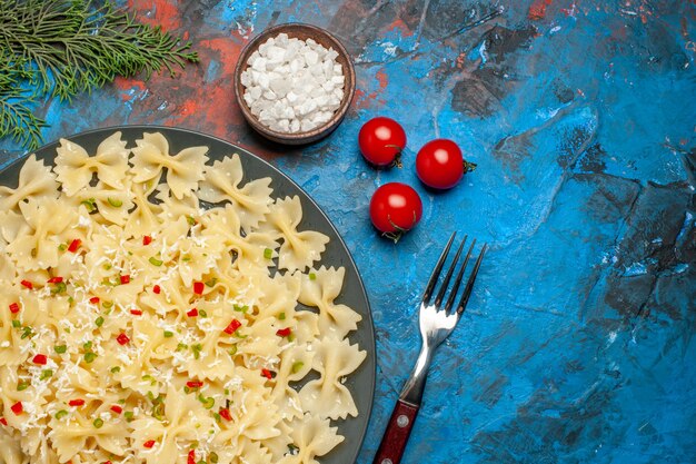 Medio tiro de pastas farfalle con verduras tomates sal y ramas de abeto de horquilla sobre fondo azul.