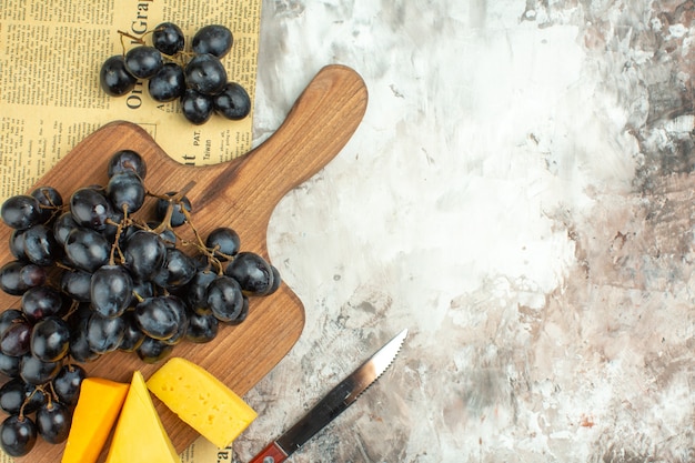 Medio tiro de racimo de uva negra deliciosa fresca y varios tipos de queso en la tabla de cortar de madera