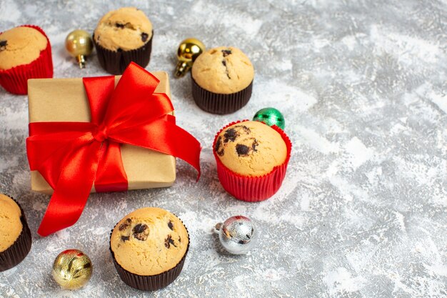 Medio tiro de regalo con cinta roja entre deliciosos cupcakes pequeños recién horneados y accesorios de decoración en la mesa de hielo