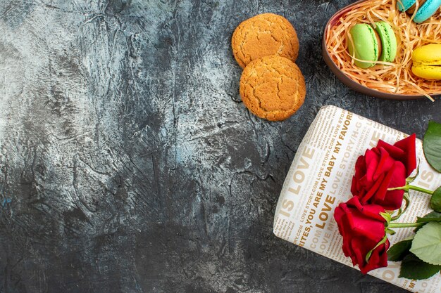 Medio tiro de rosa roja en hermosa caja de regalo con deliciosos macarons y galletas sobre fondo oscuro helado