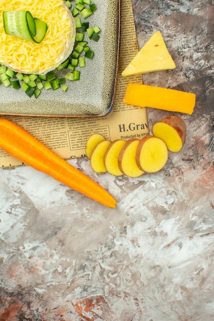 Medio tiro de sabrosa ensalada en un periódico viejo y dos tipos de queso y zanahorias, patatas picadas en la tabla de colores mezclados