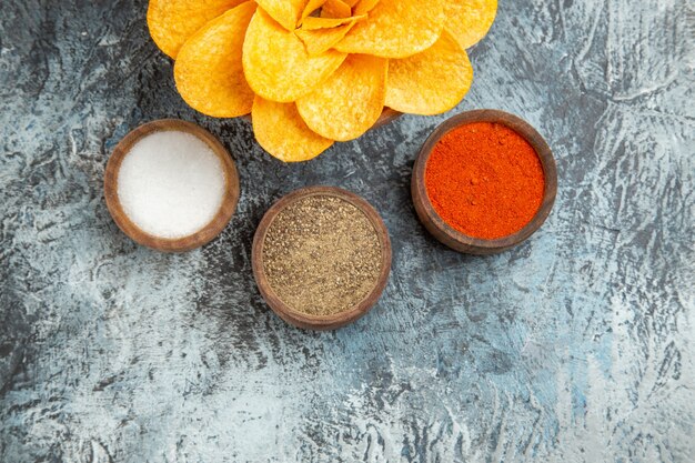 Medio tiro de sabrosas papas fritas decoradas en forma de flor y diferentes especias en mesa gris