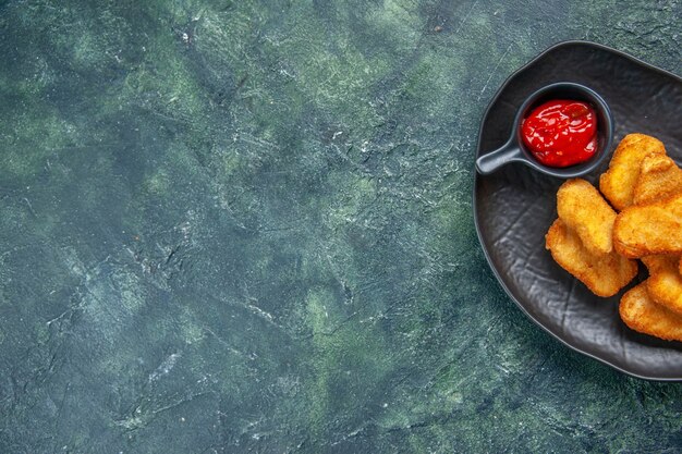 Medio tiro de sabrosos nuggets de pollo y salsa de tomate en placa negra en el lado izquierdo sobre una superficie oscura con espacio libre