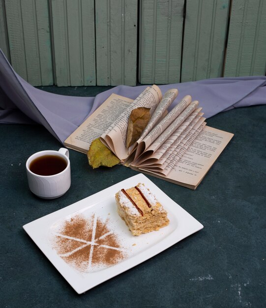 Medovik pastel con cacao en polvo y una taza de té sobre la mesa de piedra.